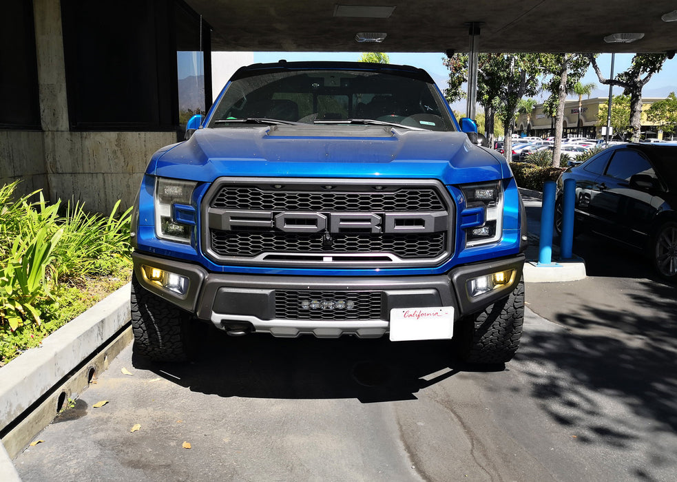 Blue Ford truck parked in a lot with trees and buildings in the background